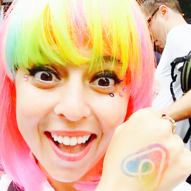 nina mufleh in a rainbow colored wig showing off the airbnb host with pride logo.